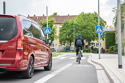 Ein Radfaher fährt vor einem roten Auto an einer Stelle, an der sich die Straße verängt und der Radschutzstreifen endet.
