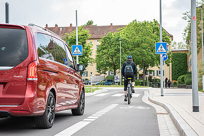 Ein Radfaher fährt vor einem roten Auto an einer Stelle, an der sich die Straße verängt und der Radschutzstreifen endet.