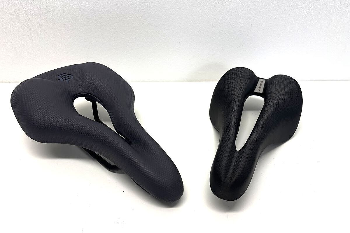 Zwei schwarze Fahrradsättel mit mittlerer Öffnung liegen nebeneinander auf einer weißen Fläche.