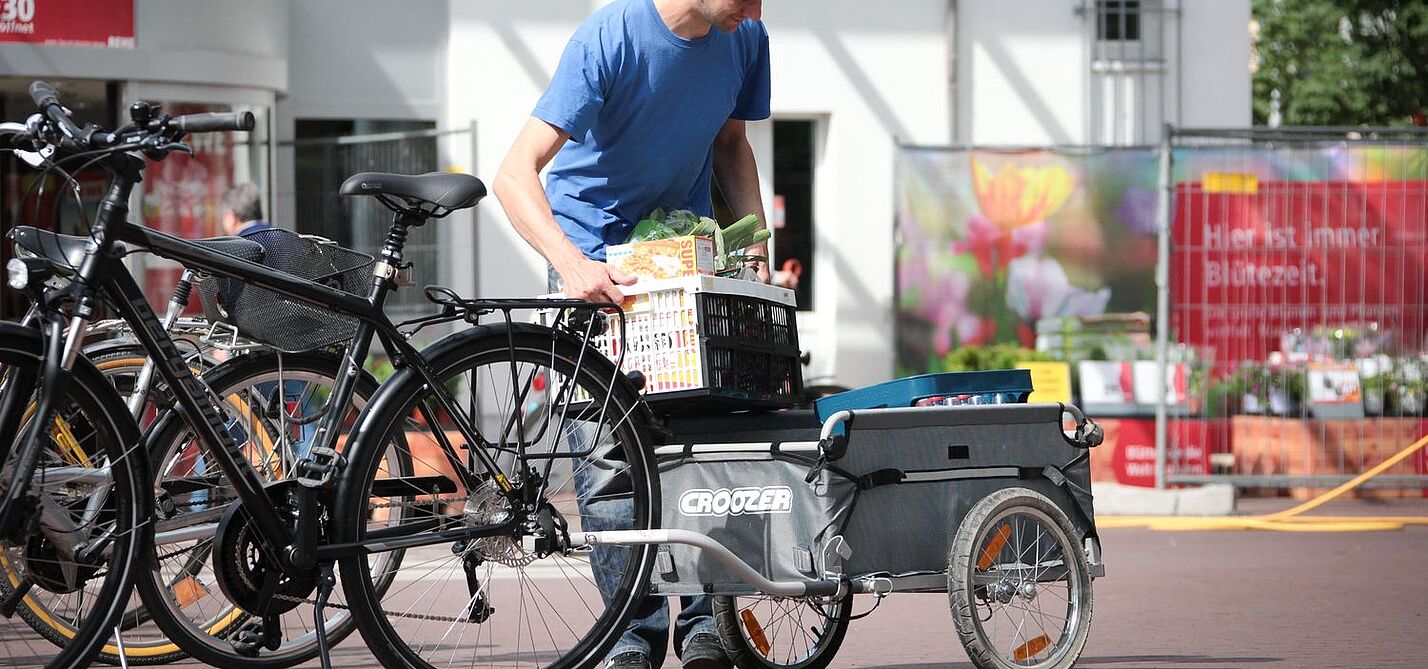 Ein Mann belädt einen Fahrradanhänger vorm Supermarkt. 