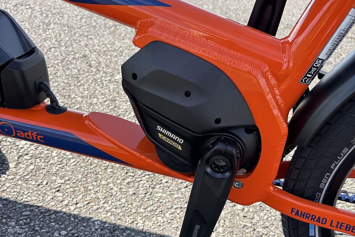 Der Motorbereich eines orangefarbenen E‑Lastenrads mit schwarzem Mittelmotor und Kurbelarm.