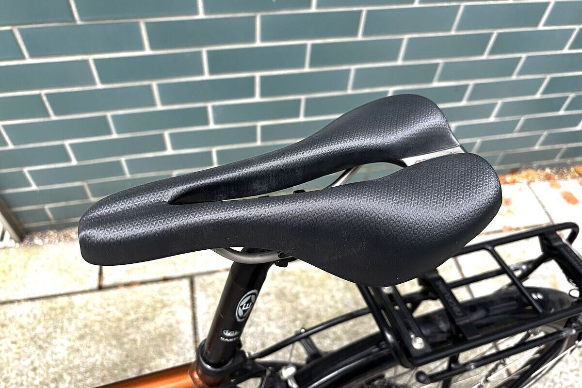 Schwarzer Fahrradsattel mit langer Öffnung, montiert an einem Fahrrad vor einer grünen Kachelwand.