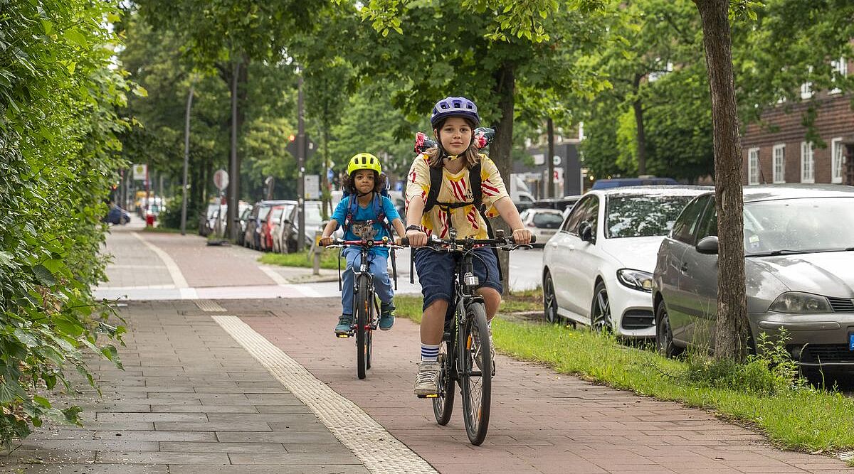 Ein Mädchen fährt vor einem Jungen auf dem Fahrrad auf einem Radweg.